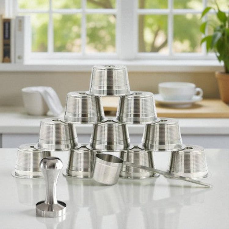 Ten single stainless steel reusable coffee pods with scoop and tamper on a kitchen countertop.
