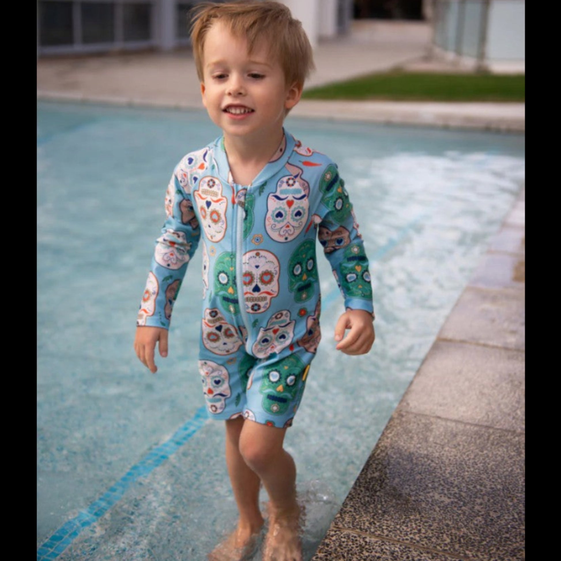 Young boy standing outdoors wearing the Tyoub aqua sugar skull print long sleeve sunsuit bather for sun smart UV protection.