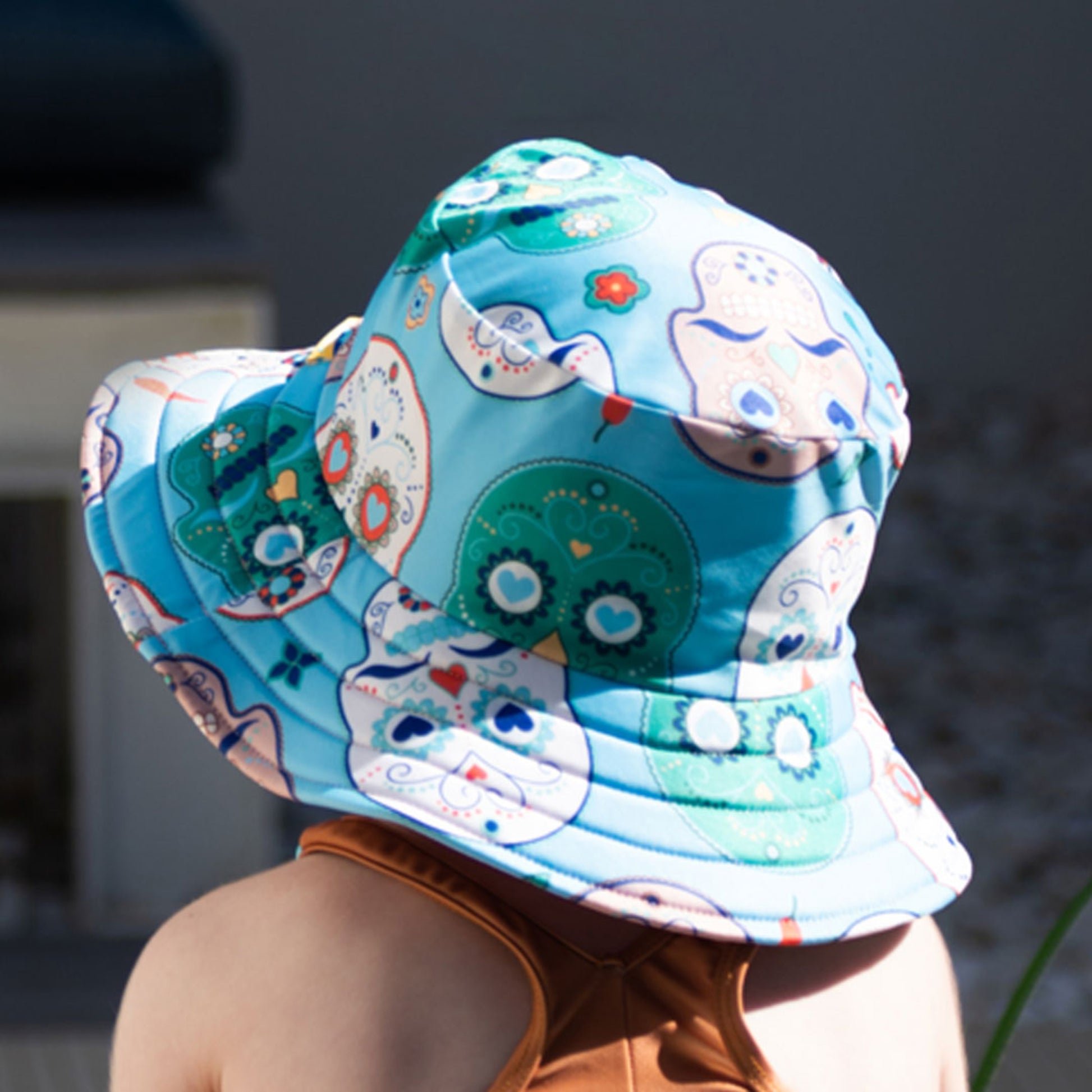 Rear view of a toddler wearing the Tyoub wide brim sun hat, highlighting the aqua sugar skull pattern and stitched brim.