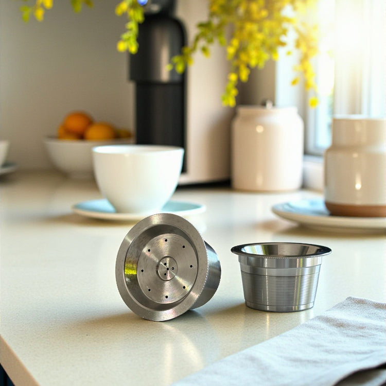 2 Reusable Stainless Steel Coffee Capsules on a kitchen bench with a coffee cup and napkin.