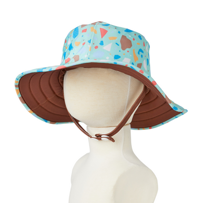 Reversible junior swim hat featuring an ocean glass terrazzo print crown with a solid turquoise  brown under-brim.