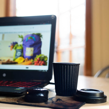 Close up view demonstrating the flexible, lightweight, and shatterproof properties of a food grade platinum cured silicone travel mug by a computer on a desk.