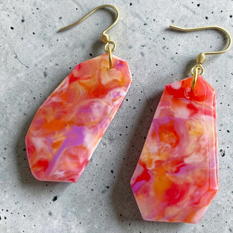 Detailed close-up of the unique color swirls and finish on the orange red recycled plastic flower dangle earrings.