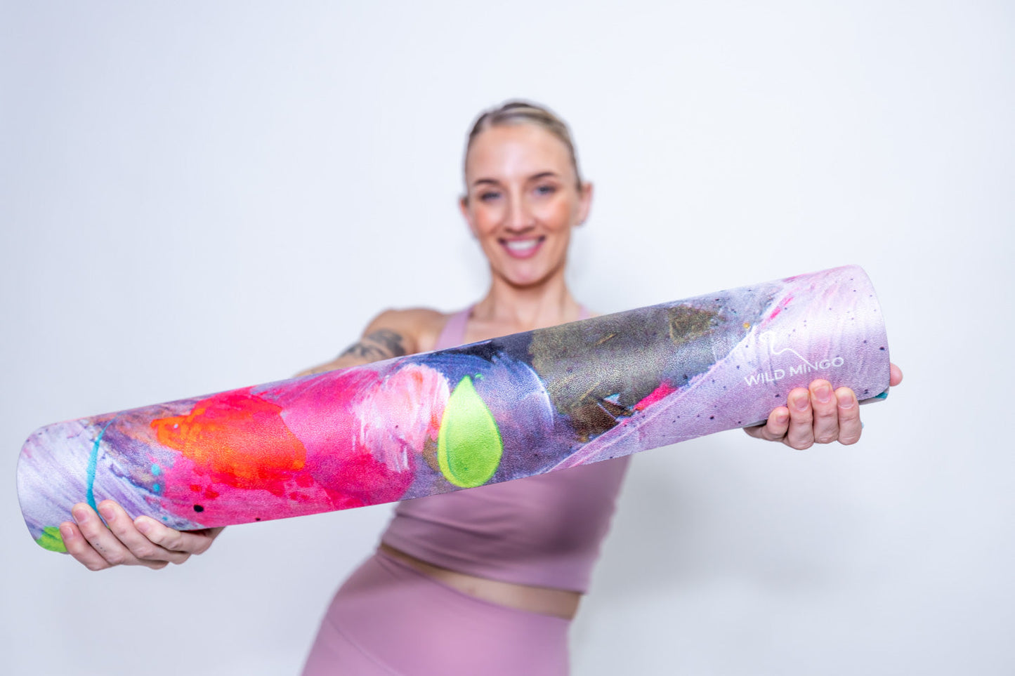 Woman holding a Flamingle Yoga Mat by Wild Mingo in a Yoga studio against a white wall